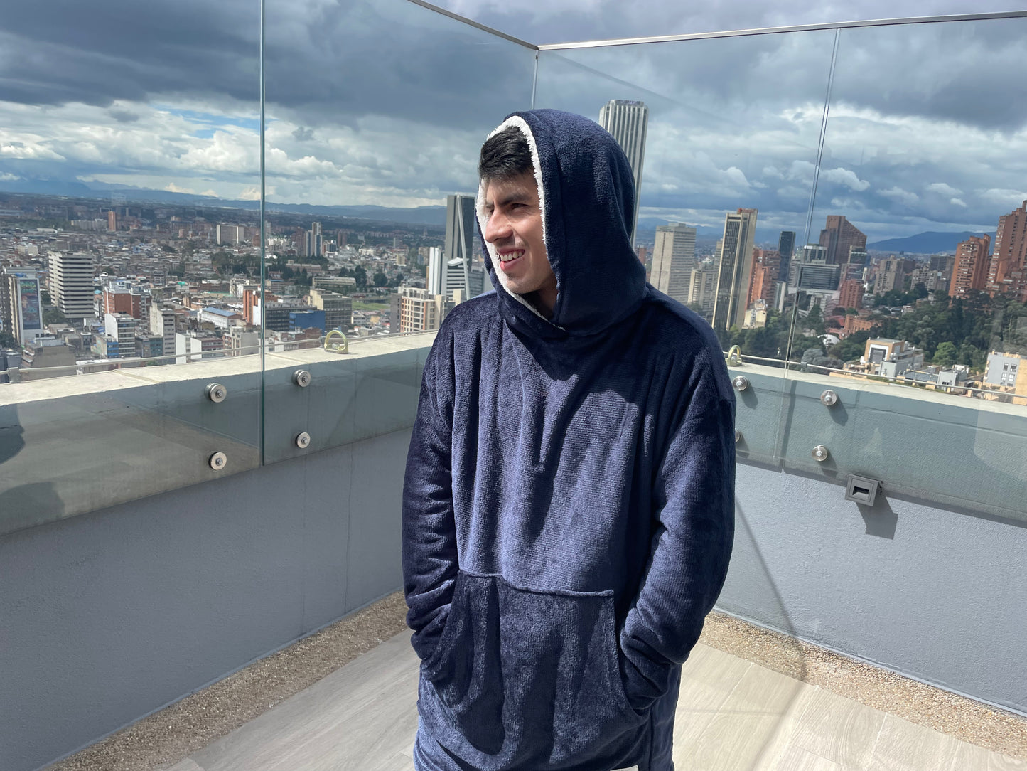 Hombre sonriendo con las manos en los bolsillos de su saco cobija azul oscuro en una terraza