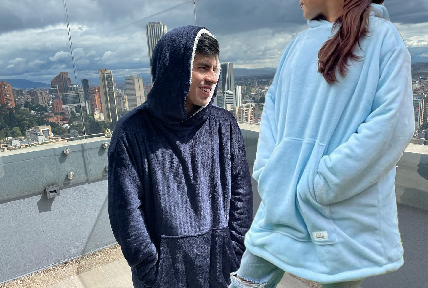Hombre sonriendo usando un saco cobija doble faz por el lado azul oscuro y mujer parada a su lado y usando el saco gigante doble faz por el lado azul claro