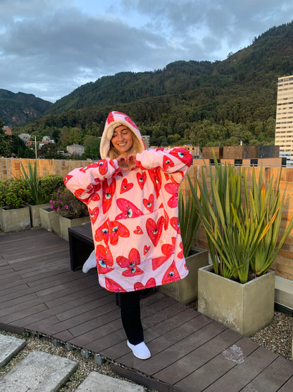 Mujer sonriente usando un saco cobija con estampado de corazones en una terraza y haciendo símbolo de corazón con sus manos