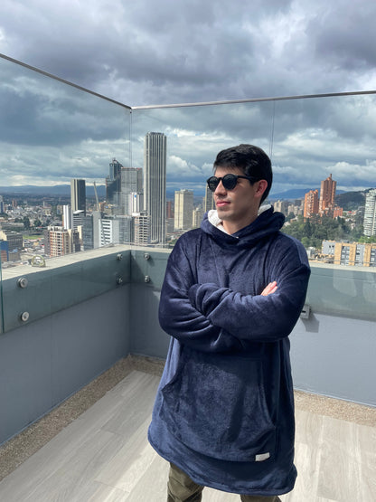 Hombre parado en una terraza usando un saco gigante azul oscuro y gafas de sol.