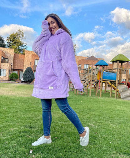 Mujer sonriente parada en un parque usando un saco cobija lila