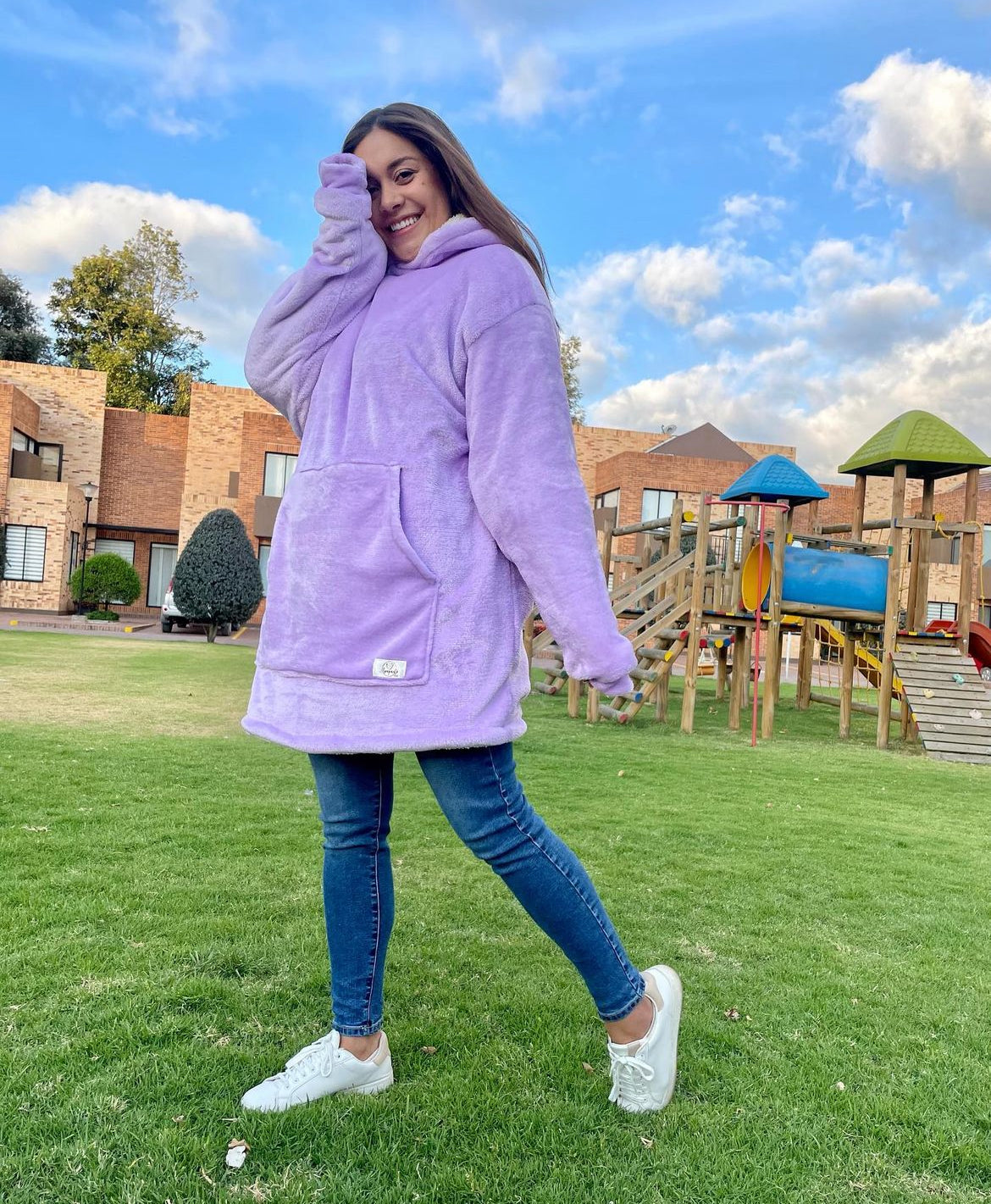 Mujer sonriente de pie en un parque usando un saco gigante color lila 