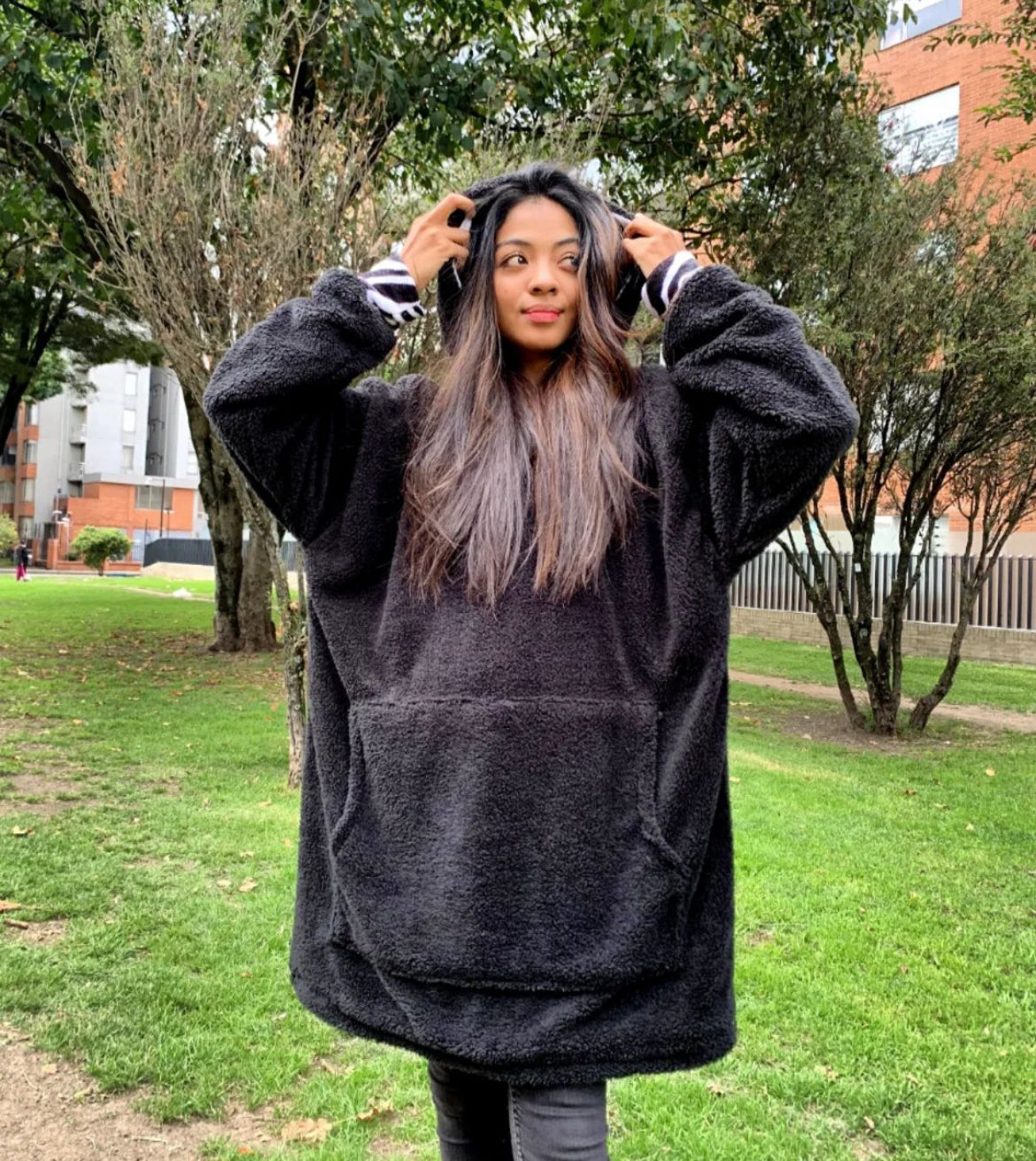 Mujer sonriente acomodando la capota de su saco gigante ovejero color negro