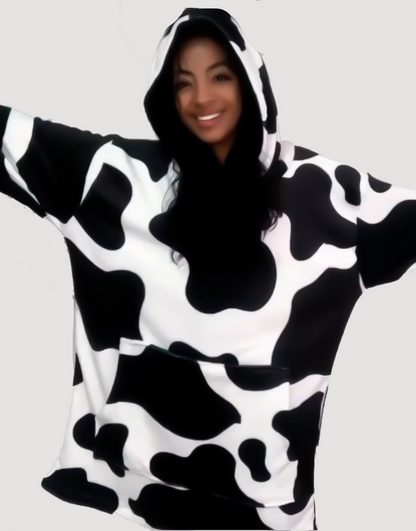 Mujer sonriendo con los brazos extendidos usando un saco cobija gigante con estampado de vaca.